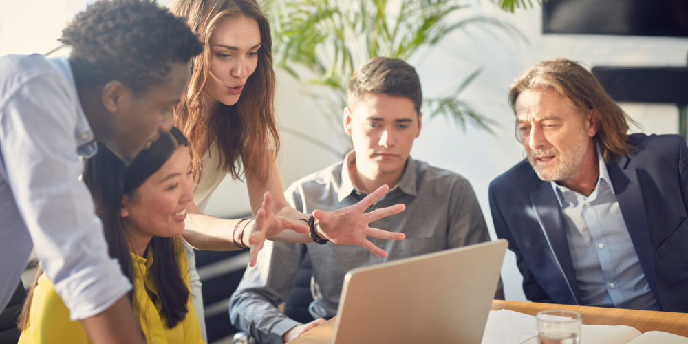Grupo diverso de profesionales en sesión de asesoría y capacitación alrededor de laptop.