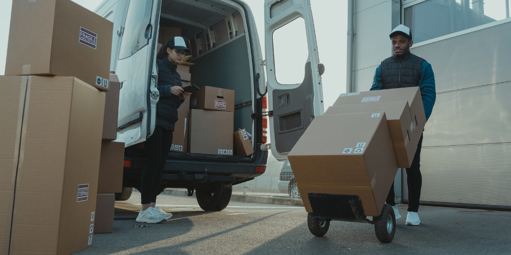 Dos profesionales cargando cajas de cartón en furgoneta de transporte. 